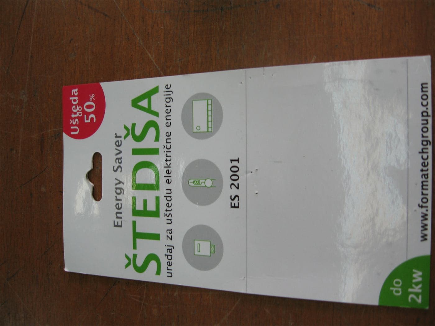 Retail packaging for an energy-saver device labelled ŠTEDIŠA ES 2001, promising fifty per cent savings, photographed on a wooden table.
